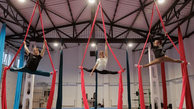 Trzy osoby wykonują szpagaty na czerwonych szarfach aerial silk