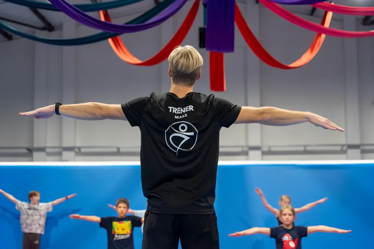 Trener prowadzi rozgrzewkę grupy dzieci w hali Akro Spot