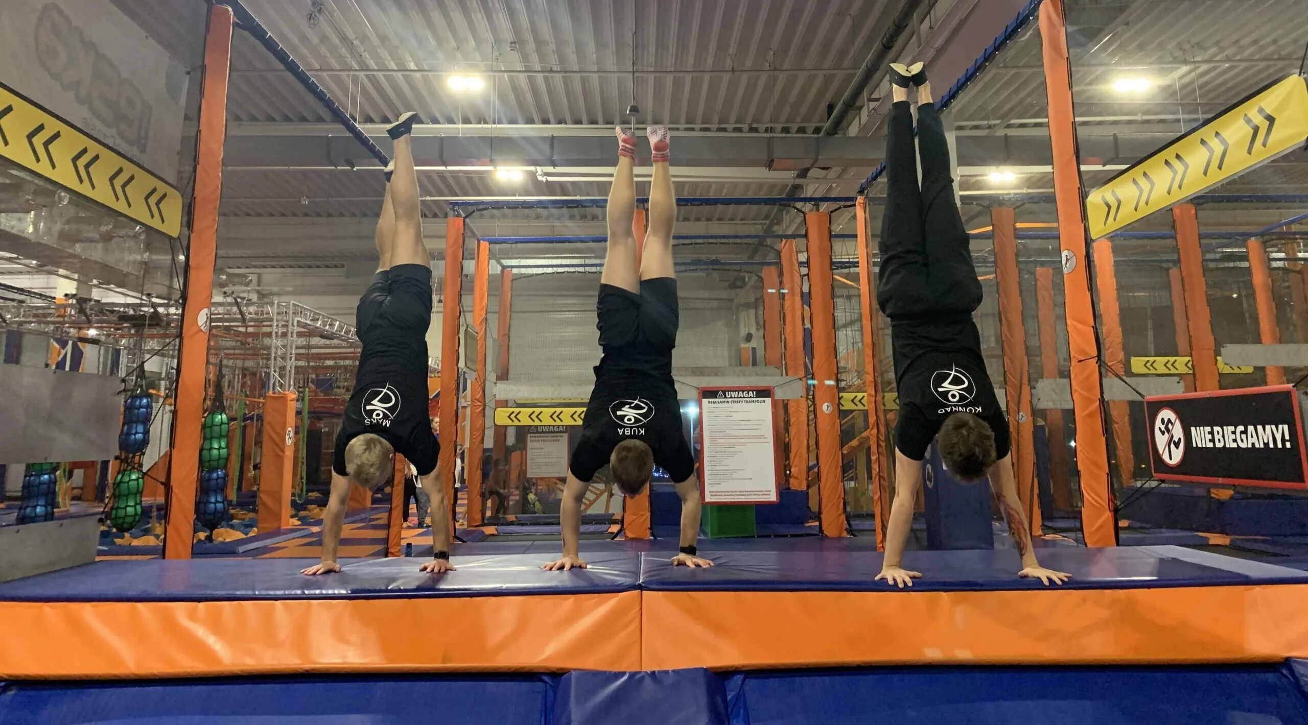 Trzy osoby stoją na rękach na trampolinach